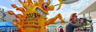 klimamonster_2_pff_foto_sandra_prufer_b.jpg Große Figur aus Pappmachée: eine Monster-Sonne tippt der personifizierten Öffentlichkeit, die wegschaut, von hinten auf die Schulter