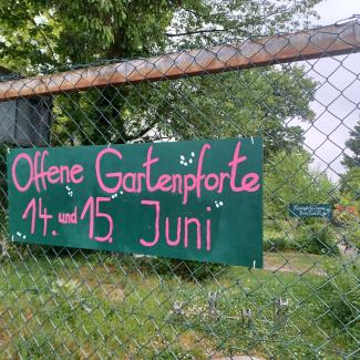 Schild mit der Aufschrift Offene Gartenpforte hängt an einem Zaun